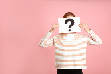 Woman holding question mark sign on pink background. Space for text