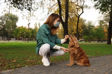 Photo of Woman in protective mask with English Cocker Spaniel in park. Walking dog during COVID-19 pandemic