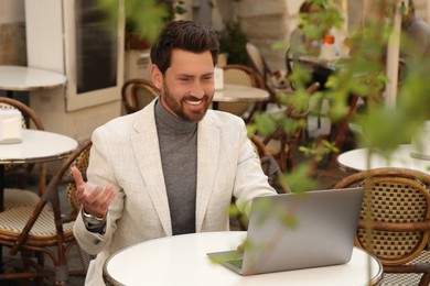 Photo of Man having video chat via laptop at table in outdoor cafe