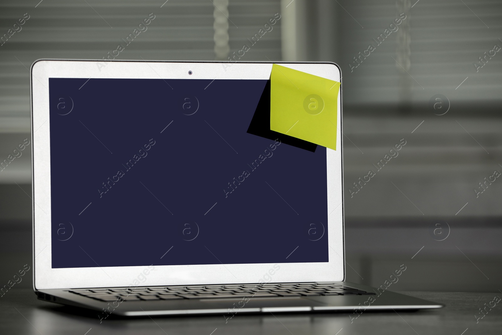 Photo of Laptop with blank sticky note on grey office desk. Space for text