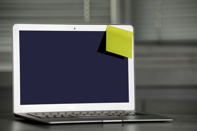 Photo of Laptop with blank sticky note on grey office desk. Space for text