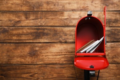 Photo of Open red letter box with envelopes against wooden background. Space for text