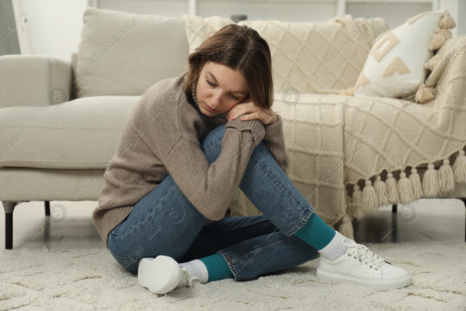 Photo of Sad young woman sitting on floor at home