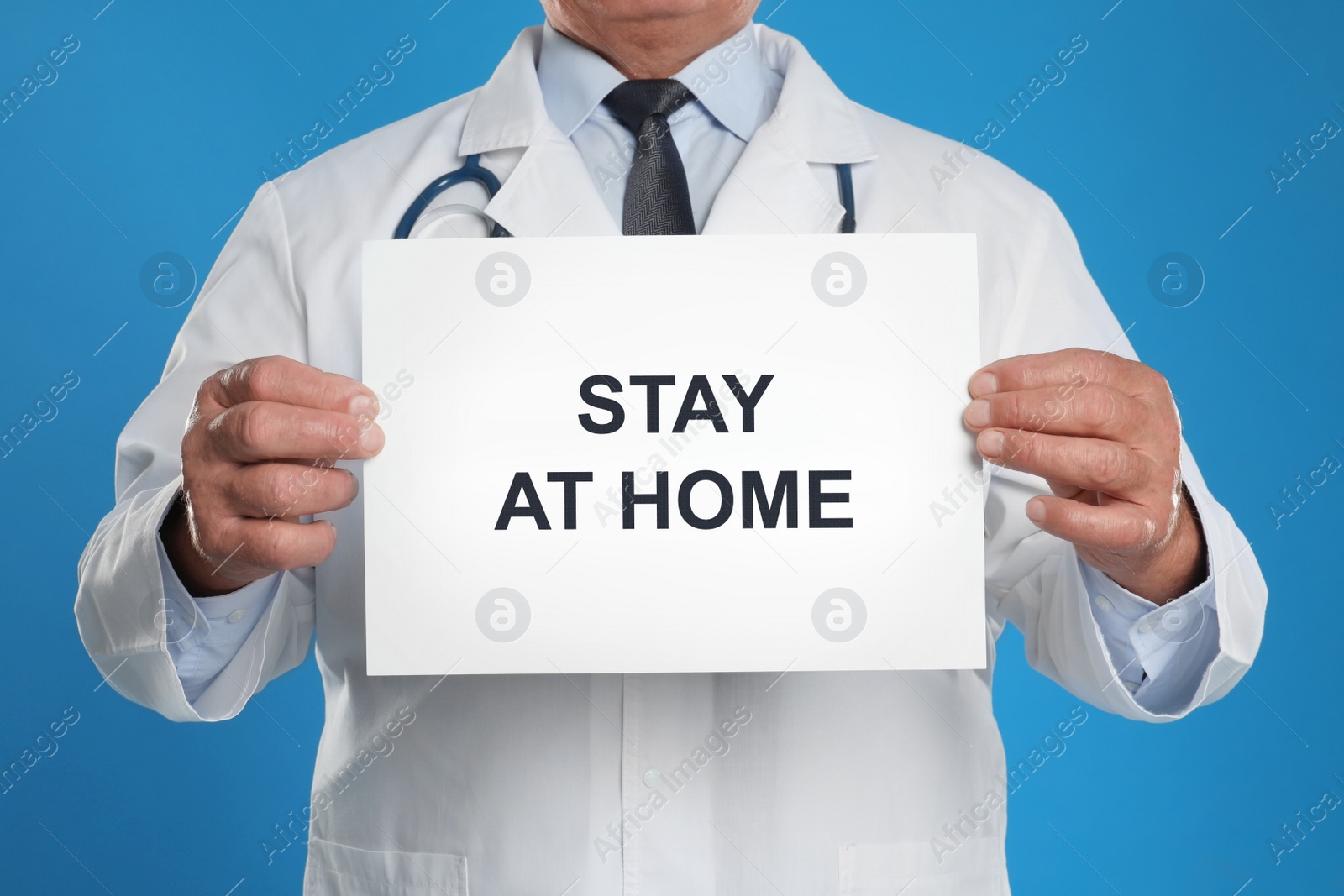 Image of Doctor holding sign with text STAY AT HOME on blue background, closeup. Quarantine during coronavirus outbreak