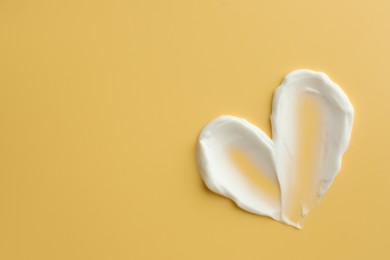 Photo of Samples of face cream in shape of heart on yellow background, top view. Space for text