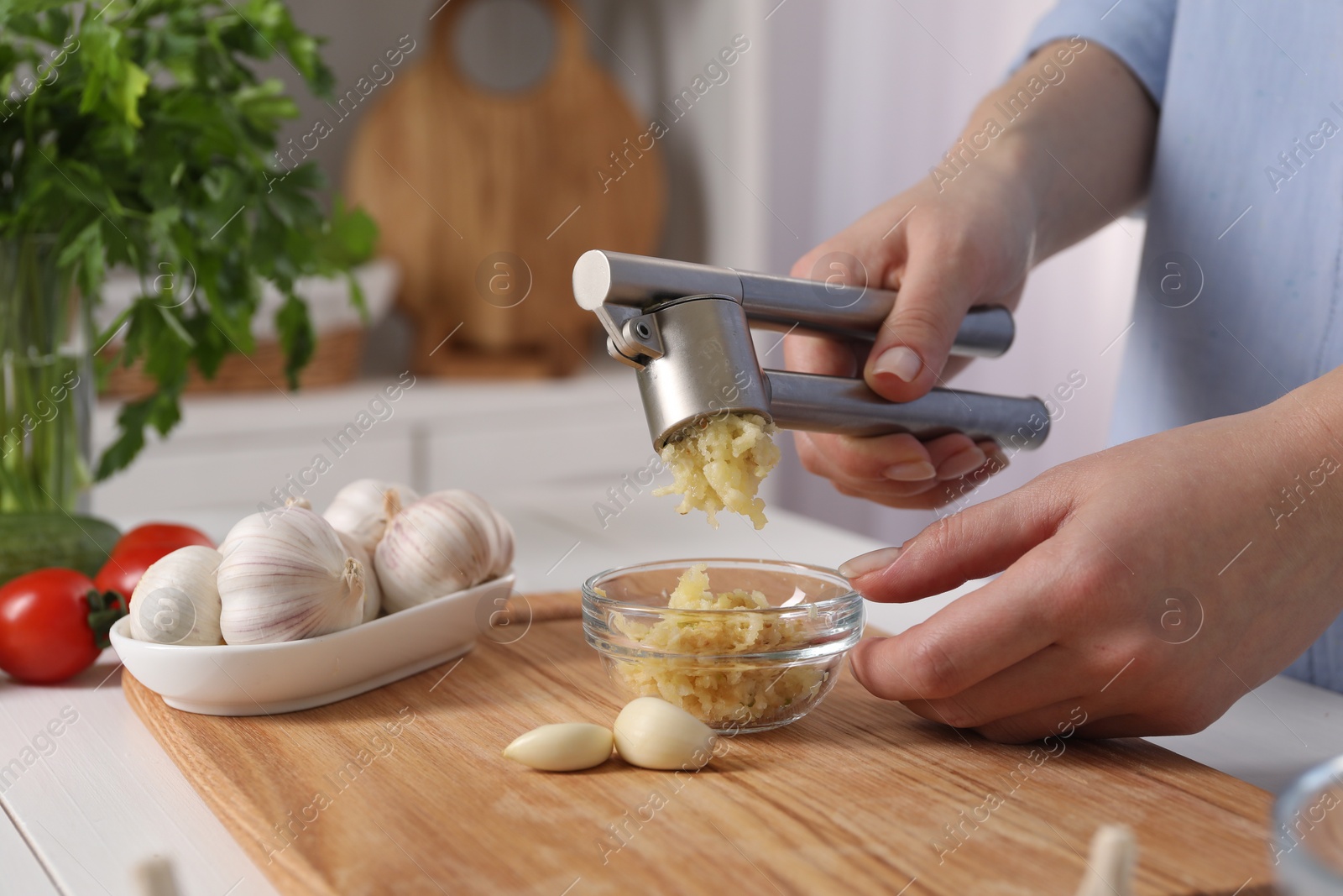 Photo of Woman squeezing garlic with press at white table in kitchen, closeup