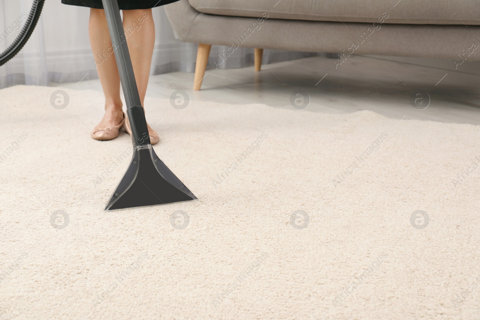 Photo of Woman removing dirt from carpet with vacuum cleaner indoors, closeup. Space for text