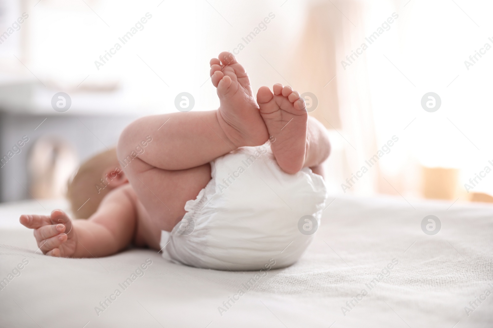 Photo of Cute little baby in diaper lying on bed in room, closeup