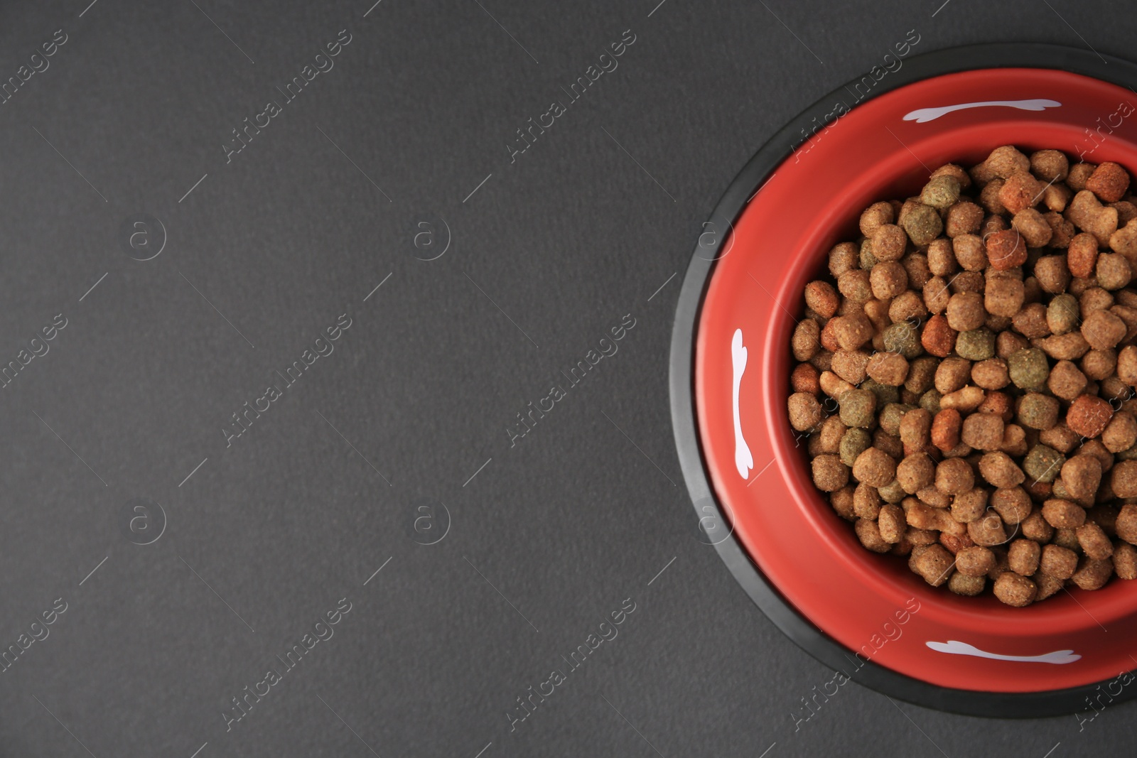 Photo of Dry dog food in feeding bowl on black background, top view. Space for text