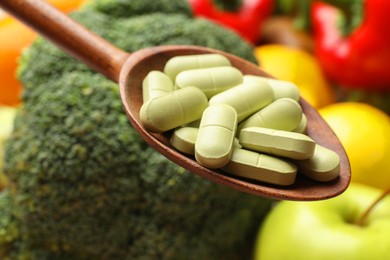 Photo of Dietary supplements. Spoon with pills over food products, closeup