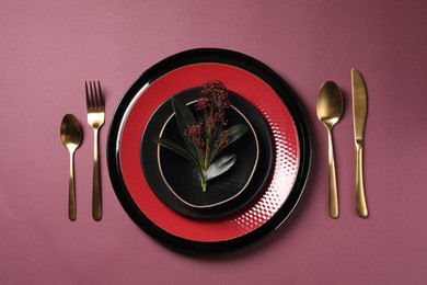 Stylish table setting with cutlery and floral decor on pink background, flat lay