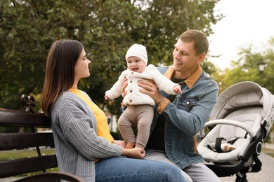 Happy parents with their adorable baby sitting on bench in park