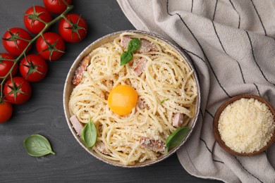 Bowl of tasty pasta Carbonara with basil leaves and egg yolk on grey wooden table, flat lay