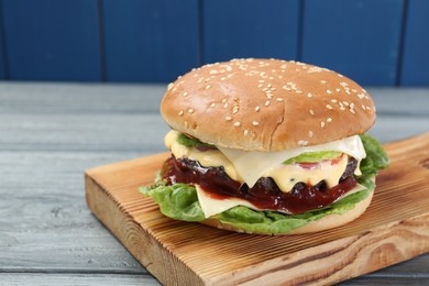 Photo of Tasty homemade cheeseburger with lettuce on grey wooden table, closeup. Space for text