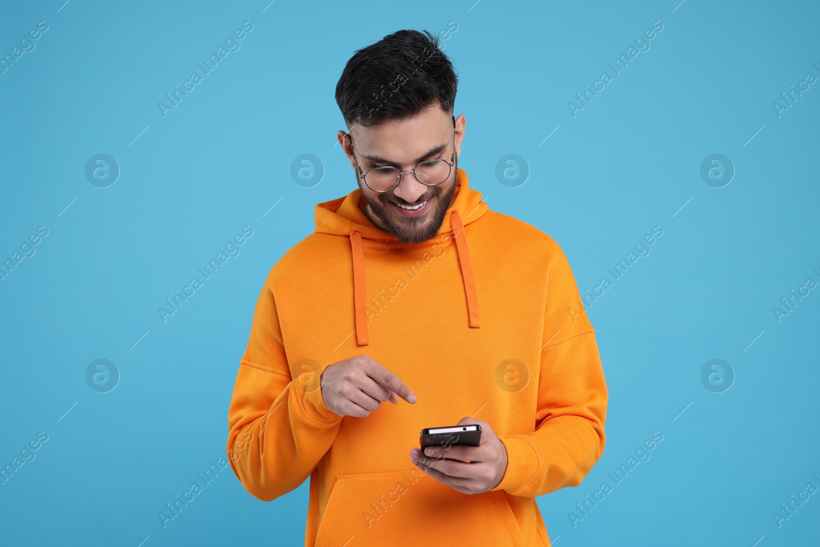 Photo of Happy young man using smartphone on light blue background