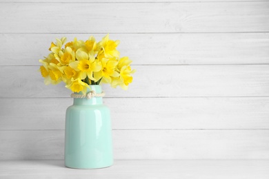 Photo of Bouquet of daffodils in vase on table against wooden background, space for text. Fresh spring flowers