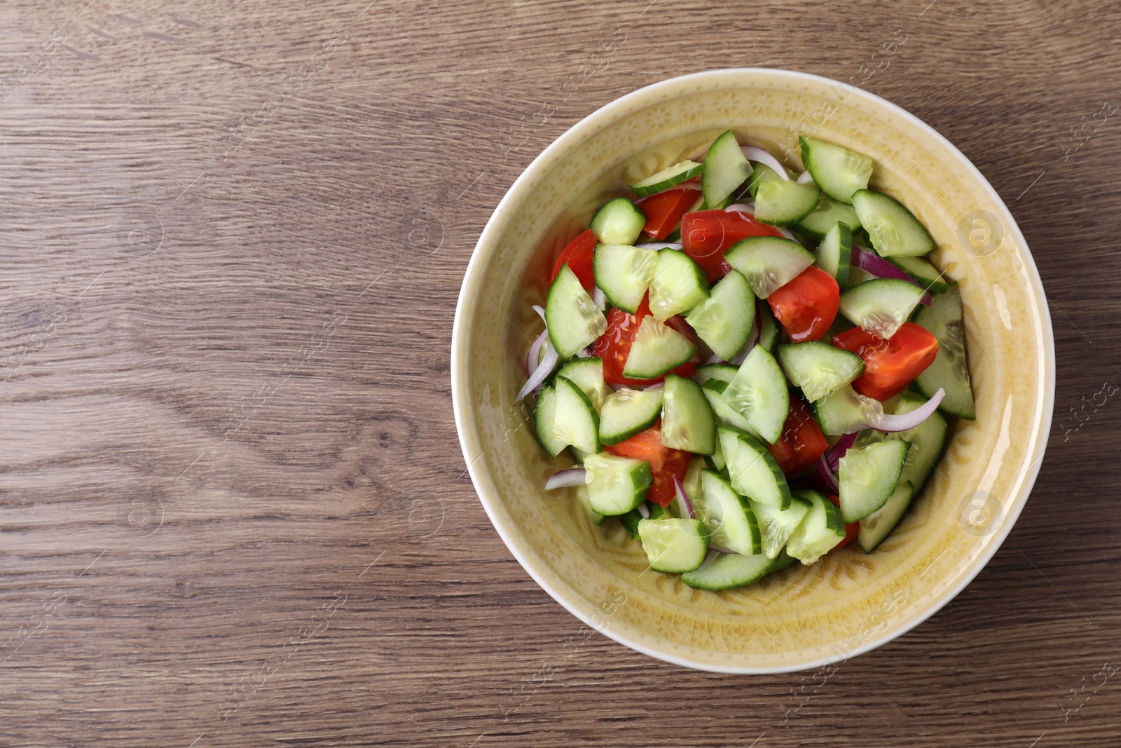 Photo of Bowl of vegetarian salad with cucumber, tomato and onion on wooden background, top view. Space for text