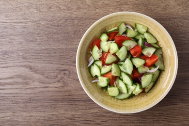 Bowl of vegetarian salad with cucumber, tomato and onion on wooden background, top view. Space for text