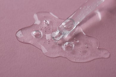 Photo of Dripping cosmetic serum from pipette onto pink background, macro view