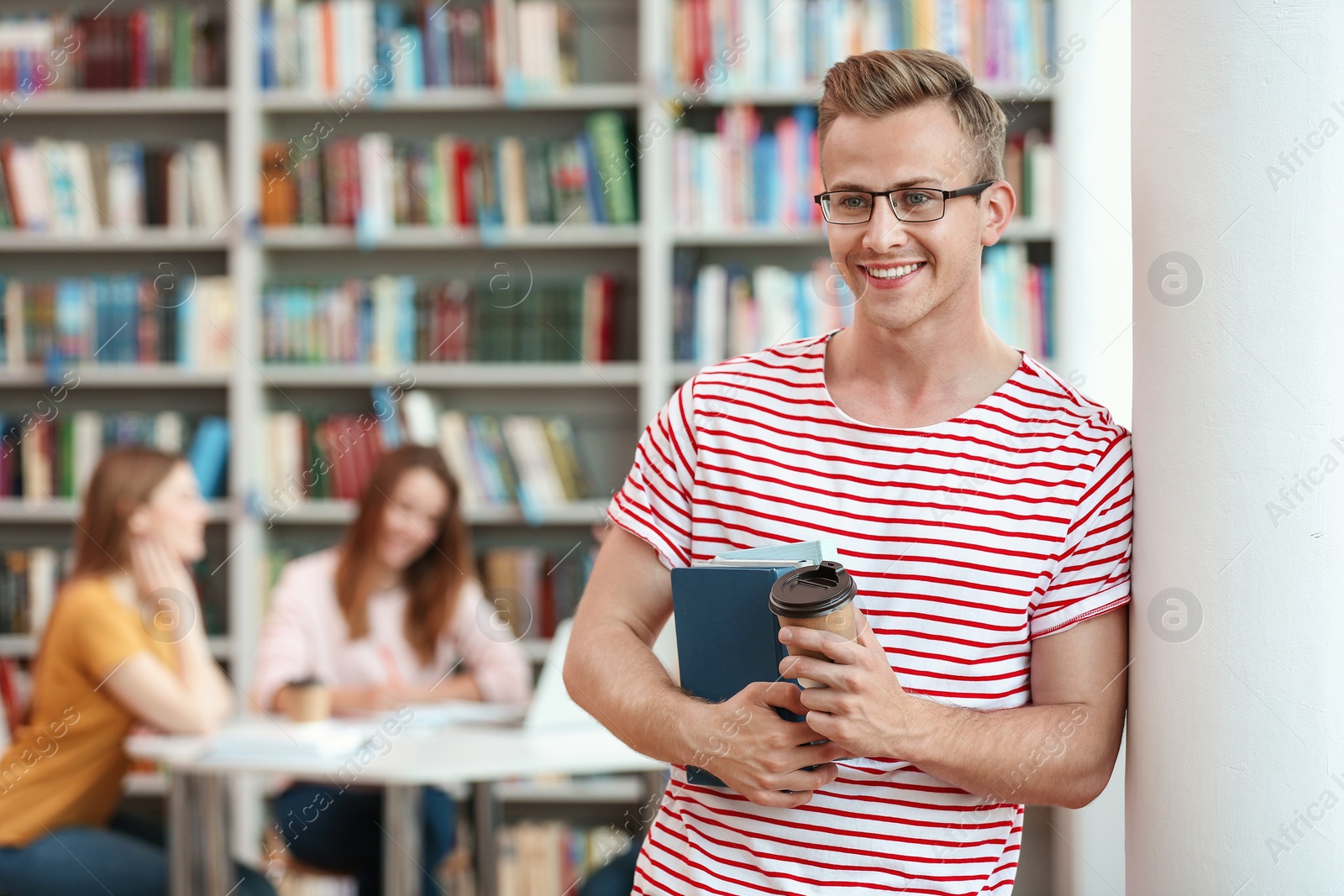 Photo of Young man with books and drink in library. Space for text