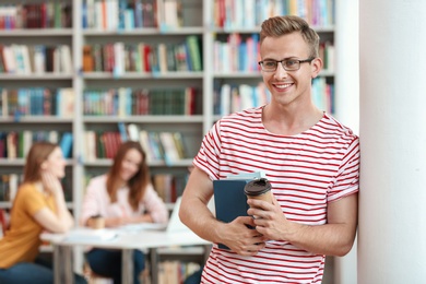 Photo of Young man with books and drink in library. Space for text