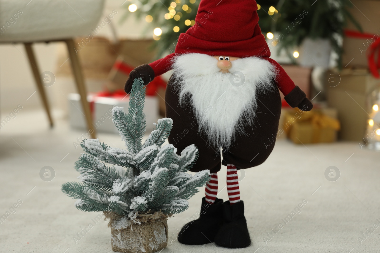 Photo of Funny Christmas gnome and tree on floor in room with festive decoration