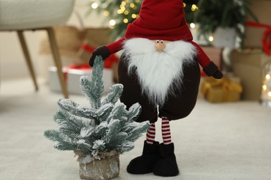 Photo of Funny Christmas gnome and tree on floor in room with festive decoration