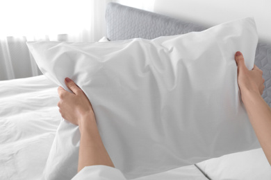 Photo of Woman fluffing soft pillow in bedroom, closeup
