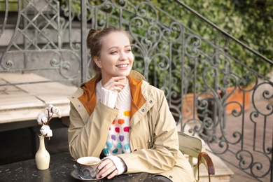 Young woman enjoying tasty coffee at table outdoors