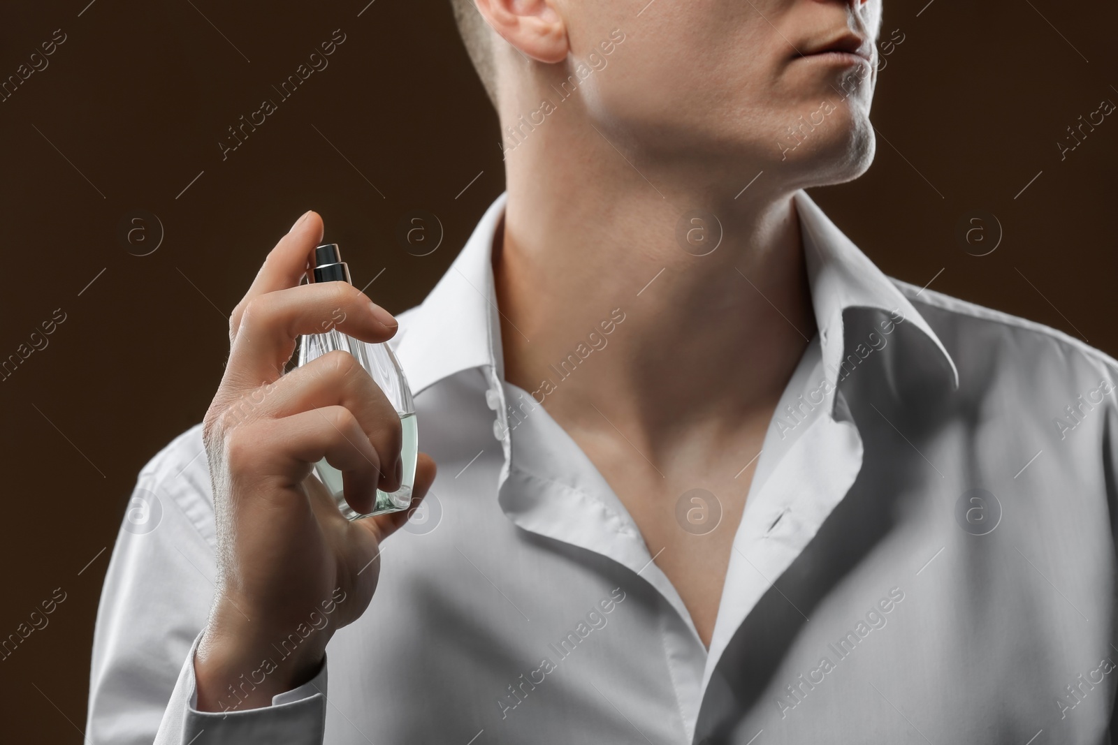 Photo of Handsome man in shirt using perfume on dark background, closeup