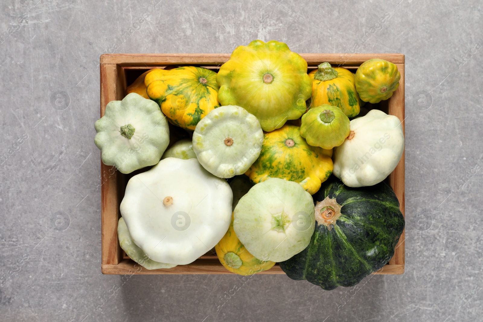 Photo of Fresh ripe pattypan squashes in wooden crate on light grey table, top view