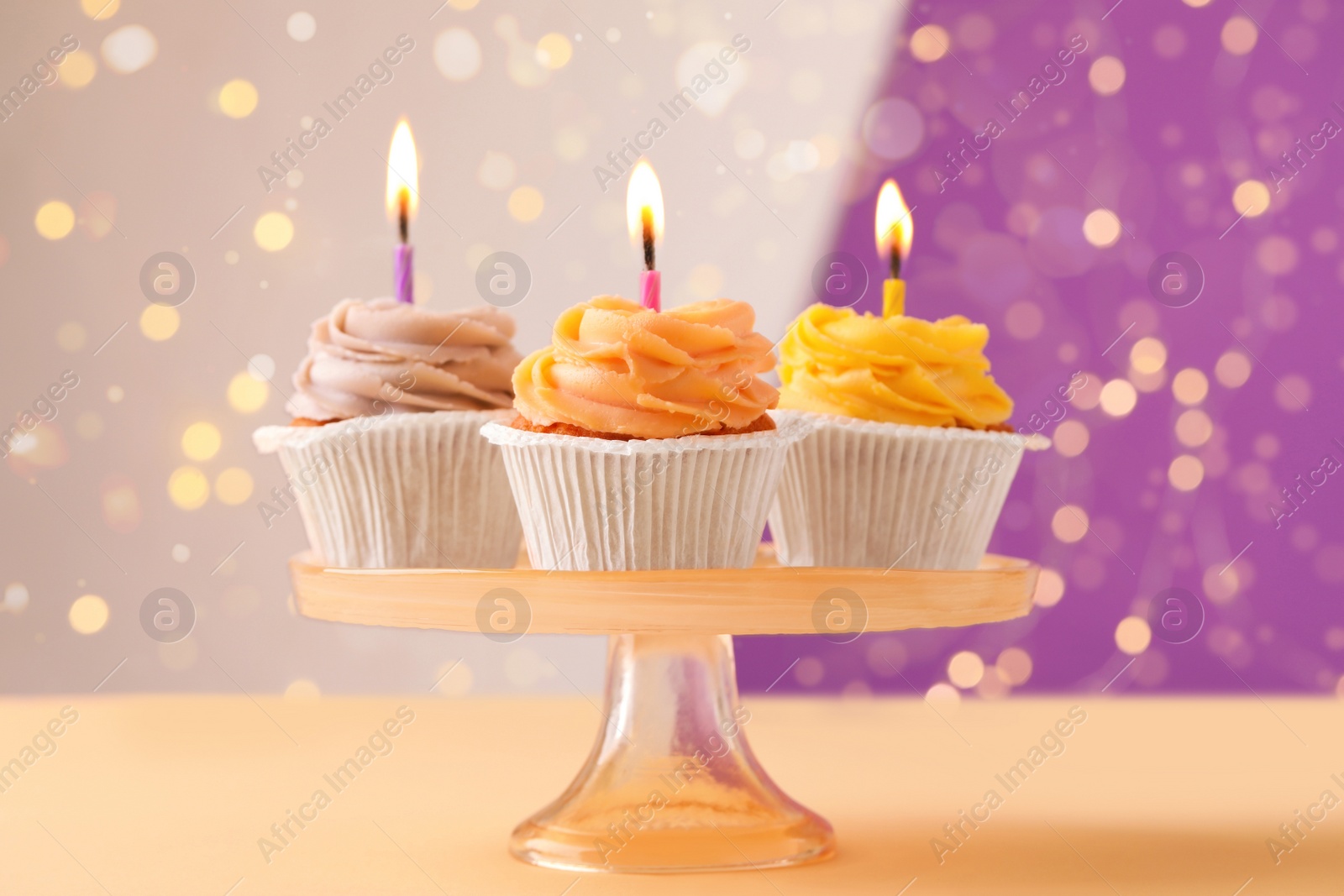 Photo of Stand with birthday cupcakes on table against blurred lights