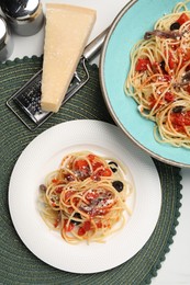 Delicious pasta with anchovies, tomatoes and parmesan cheese served on white table, flat lay