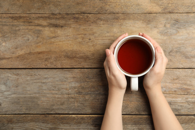 Photo of Woman with cup of tea at wooden table, top view. Space for text