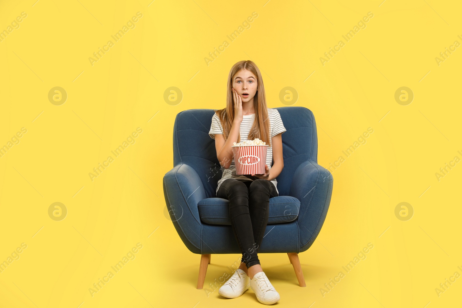 Photo of Emotional teenage girl with popcorn sitting in armchair during cinema show on color background