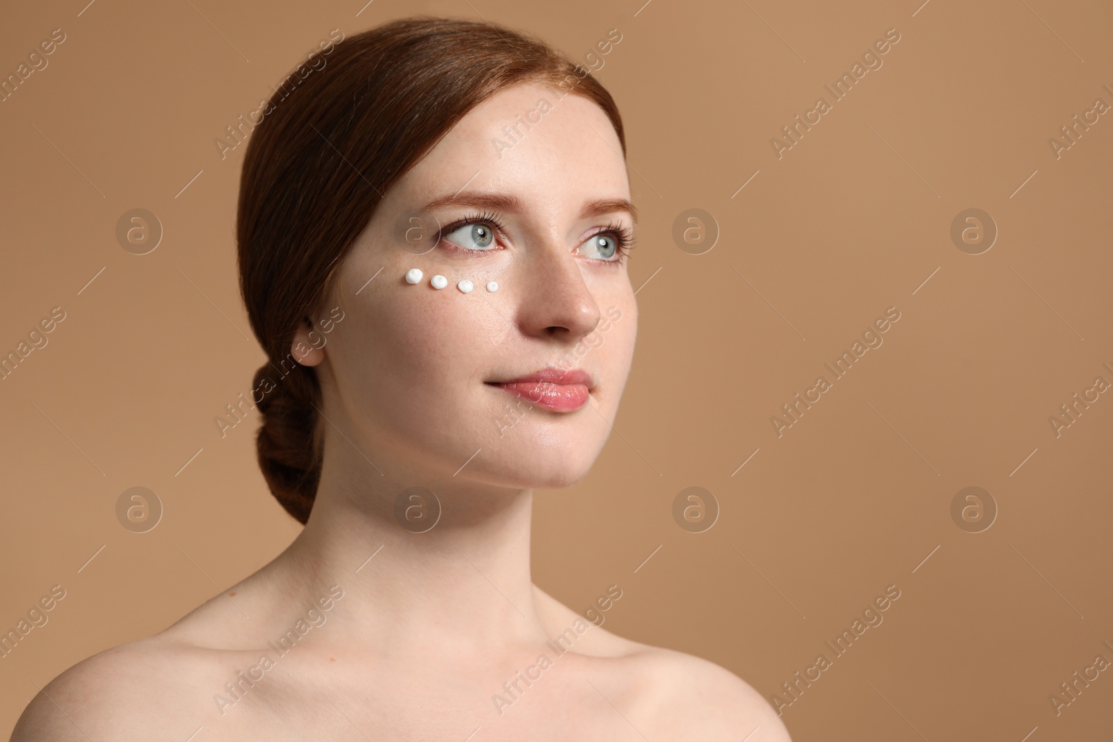 Photo of Beautiful woman with freckles and cream on her face against beige background. Space for text