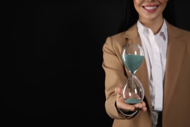 Photo of Businesswoman holding hourglass on black background, closeup with space for text. Time management