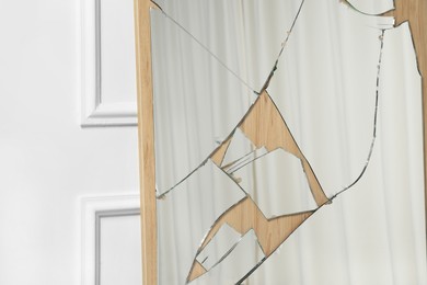 Photo of Broken mirror with many cracks near white wall, closeup