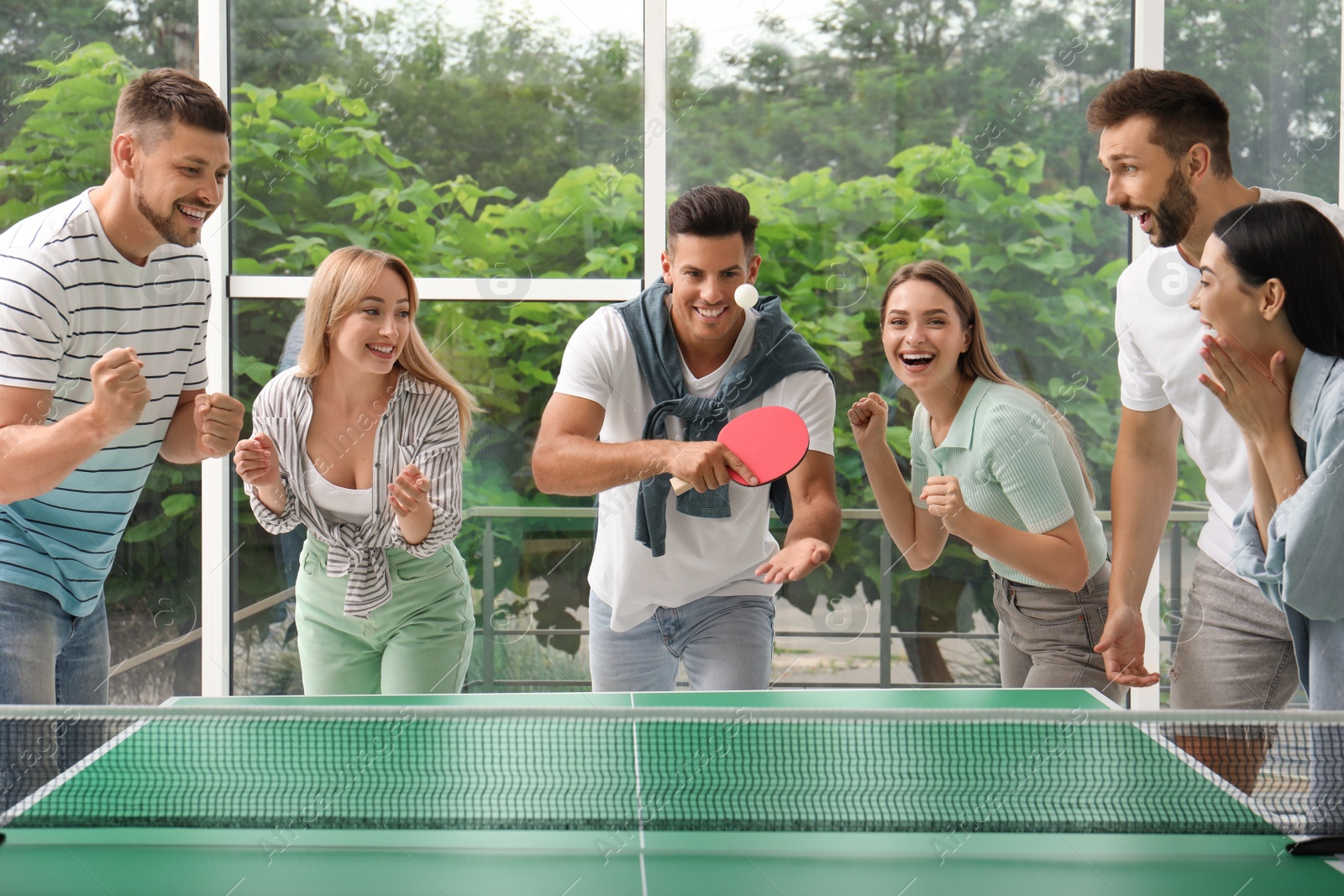 Photo of Happy friends playing ping pong together indoors