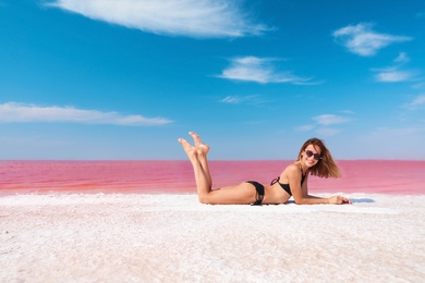 Photo of Beautiful woman in swimsuit lying near pink lake on sunny day