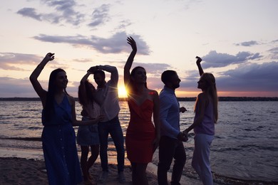Photo of Group of friends having fun near river at sunset. Summer party
