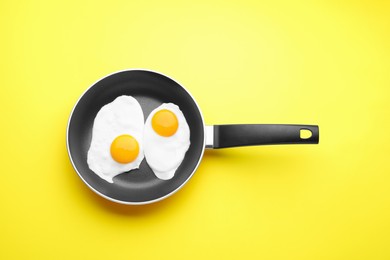 Photo of Tasty fried eggs in pan on yellow background, top view