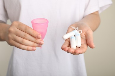 Woman holding menstrual cup and tampons on light background, closeup