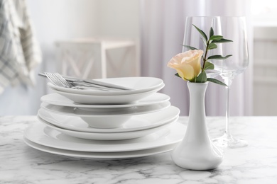 Photo of Set of clean dishes and vase with flower on white marble table