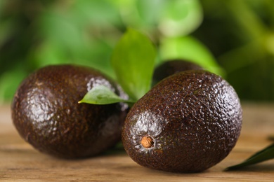 Whole avocados with green leaf on wooden table, closeup