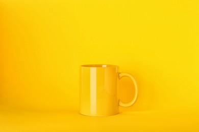 Photo of New blank ceramic mug on yellow background