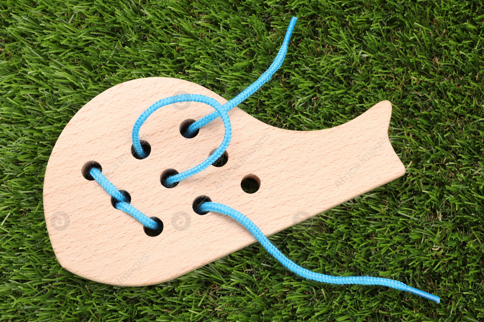 Photo of Wooden whale figure with holes and lace on artificial grass, top view. Educational toy for motor skills development