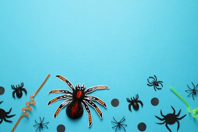 Photo of Flat lay composition with spiders, confetti and straws on light blue background, space for text. Halloween celebration