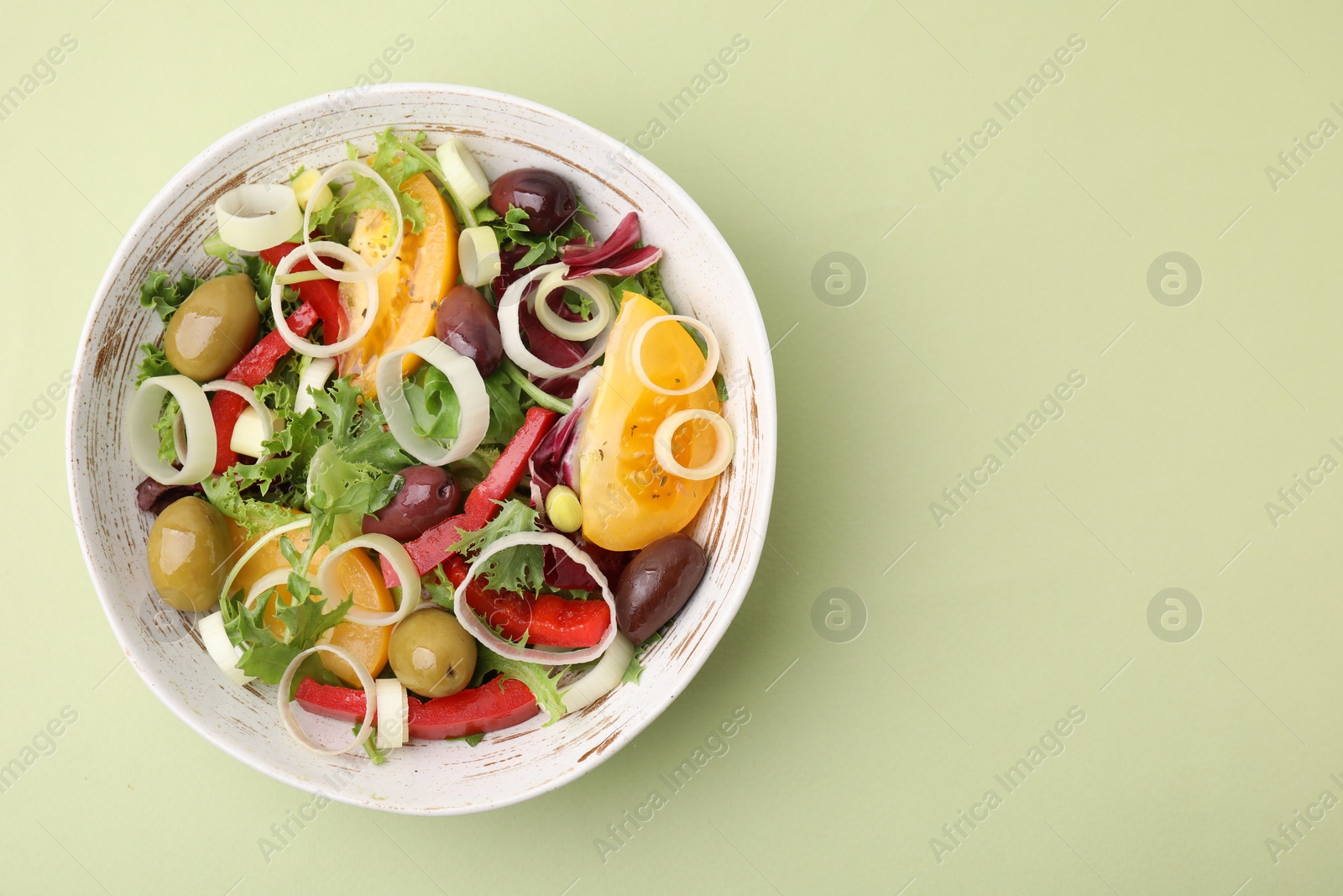 Photo of Bowl of tasty salad with leek and olives on light green table, top view. Space for text