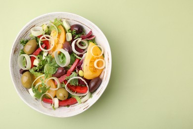 Bowl of tasty salad with leek and olives on light green table, top view. Space for text